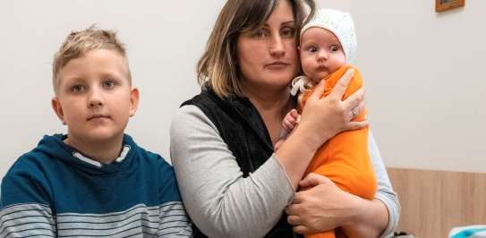 Picture of a woman holding a baby, with her son sitting next to her in a church shelter in Ukraine